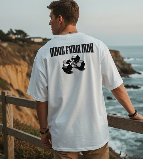 Person wearing a white T-shirt with a bold back design that reads “Made From Iron” in strong, block lettering above an illustration of two black dumbbells. The graphic captures a powerful, fitness-inspired aesthetic, perfect for gym enthusiasts, weightlifters, and strength training fans who want to showcase their dedication and passion for lifting.