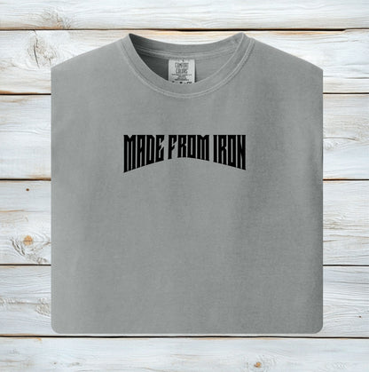 Person wearing a granite T-shirt featuring the bold text “MADE FROM IRON” in a strong, arched black font across the chest. The design conveys strength, resilience, and determination, making it perfect for fitness enthusiasts, bodybuilders, and athletes who embrace a powerful mindset. Casual streetwear style with a rugged, motivational vibe ideal for workouts, training, or everyday wear.