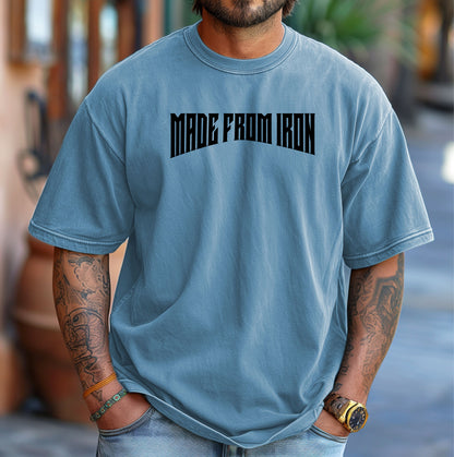 Person wearing a washed denim T-shirt featuring the bold text “MADE FROM IRON” in a strong, arched black font across the chest. The design conveys strength, resilience, and determination, making it perfect for fitness enthusiasts, bodybuilders, and athletes who embrace a powerful mindset. Casual streetwear style with a rugged, motivational vibe ideal for workouts, training, or everyday wear.