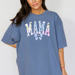 Person wearing a blue jean T-shirt featuring the word “MAMA” in large block letters filled with a delicate blue hydrangea floral pattern, accented with soft green and pink tones. Below the text is a pastel blue coquette bow, adding a sweet, feminine touch.  This spring-inspired graphic tee blends floral elegance with playful charm, perfect for fashionable moms.