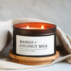 Mango + Coconut Milk candle in a 8 oz black matte candle tin on a wooden coaster with a beige cloth background