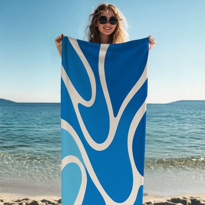 Woman holding a beach towel with a modern abstract wave design in vibrant shades of blue and white. The curvy, fluid pattern evokes ocean movement, making it the perfect stylish and eye-catching accessory for summer beach days, poolside lounging, or tropical getaways.