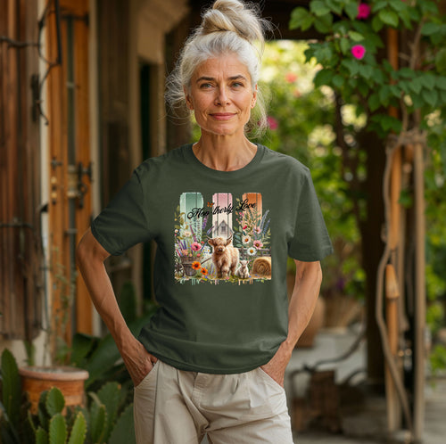 Hemp color “Moo-therly Love” T-shirt featuring a charming highland cow with her calf, surrounded by colorful wildflowers, greenery, and rustic farm elements. The background showcases three vertical distressed panels in green, cream, and orange, with a quaint barn and butterfly detail. This soft, casual tee blends country charm with sweet, pastoral style, perfect for animal lovers and farm-inspired fashion.