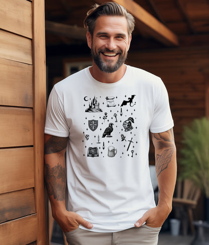 Man wearing a white T-shirt featuring the "Moonlit Magick" Renaissance Faire design. The shirt showcases a collection of detailed black illustrations, including a medieval castle, a dragon, knight helmet, shield, raven, spellbook, sword, key, mug of ale, and stars—capturing the enchanting spirit of medieval fantasy.