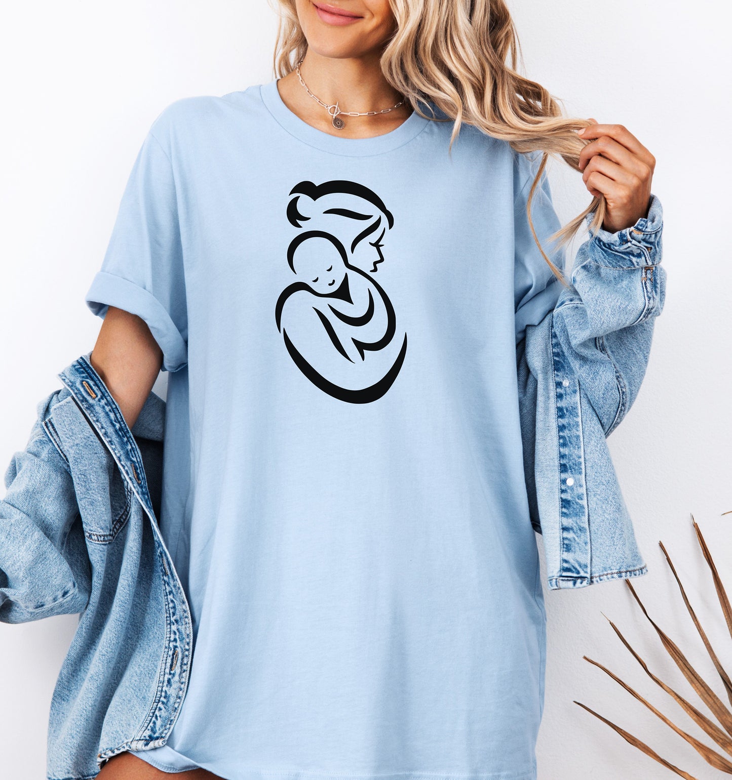 Baby blue t-shirt with a black graphic of a Mother and Child worn by a person, with a denim jacket.