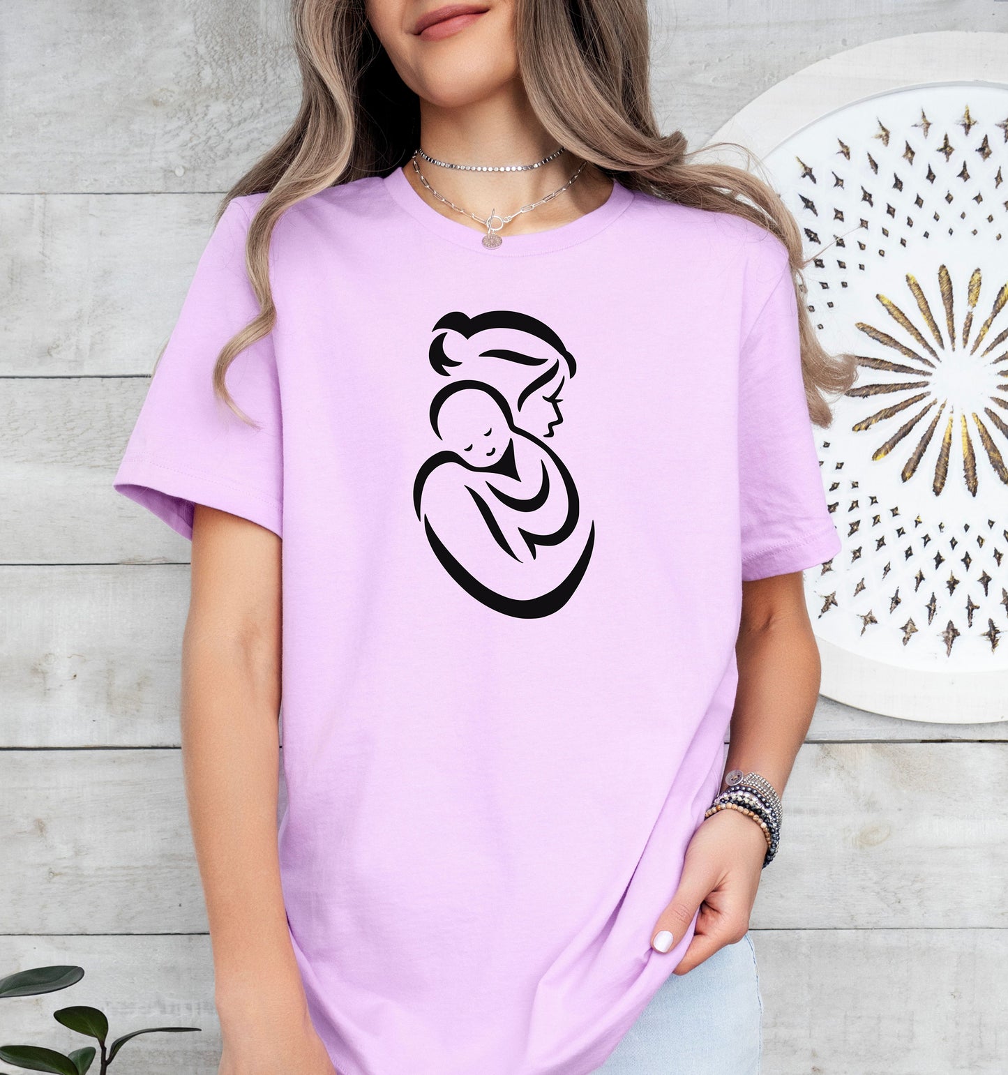 Person wearing a lilac t-shirt with a black Mother and Child graphic design against a light wooden background