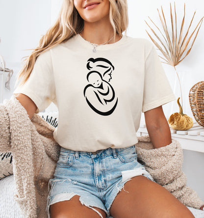 Person wearing a natural t-shirt with a black Mother and Child graphic, sitting on a couch.