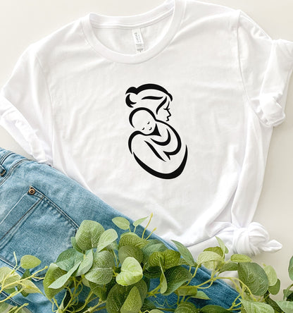 White t-shirt with a black Mother and Child graphic of a woman holding a baby, placed on blue jeans with green leaves.