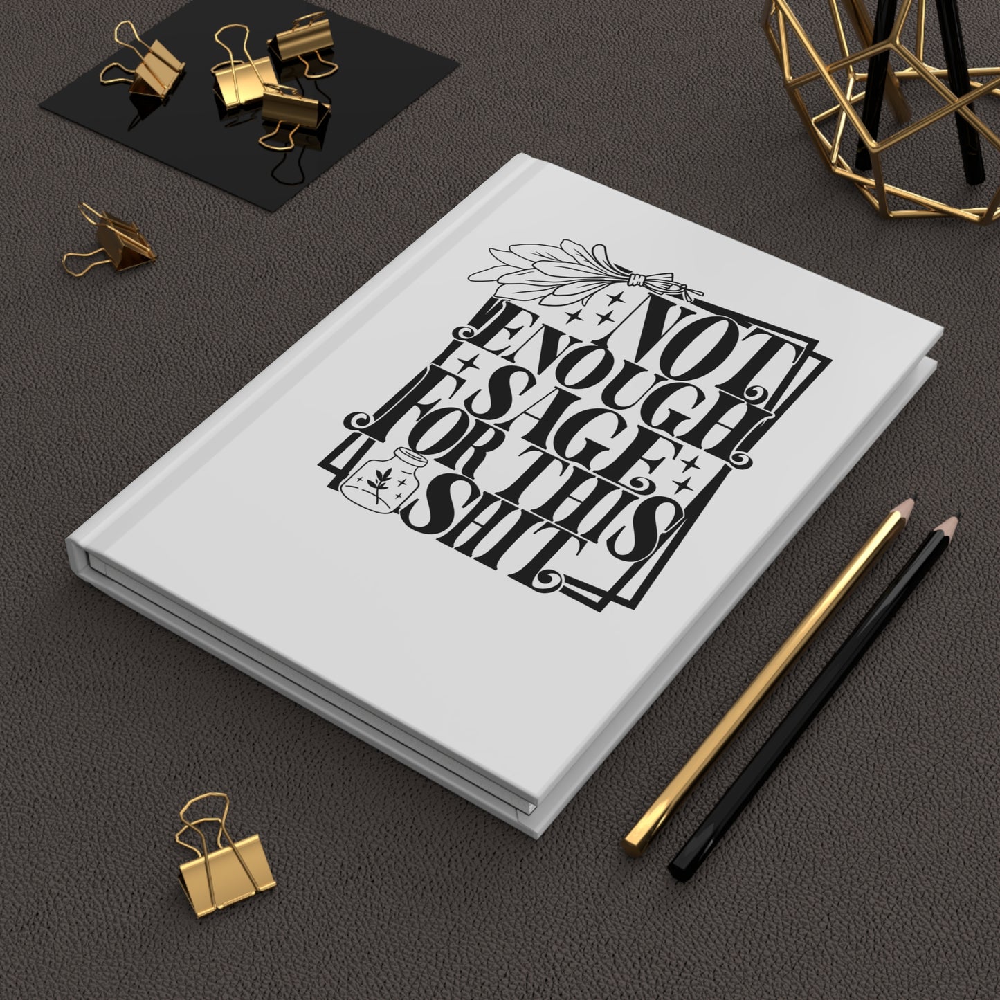 Hardcover Journal with black text design on a dark surface with office supplies.