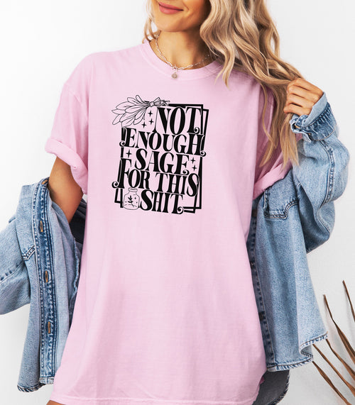 Blossom pink T-shirt with bold black typography reading “Not Enough Sage For This Shit,” accented with illustrated sage leaves, sparkles, and a small potion jar with a leafy design. Playful and cheeky statement shirt for spiritual, witchy, or humor-loving personalities.