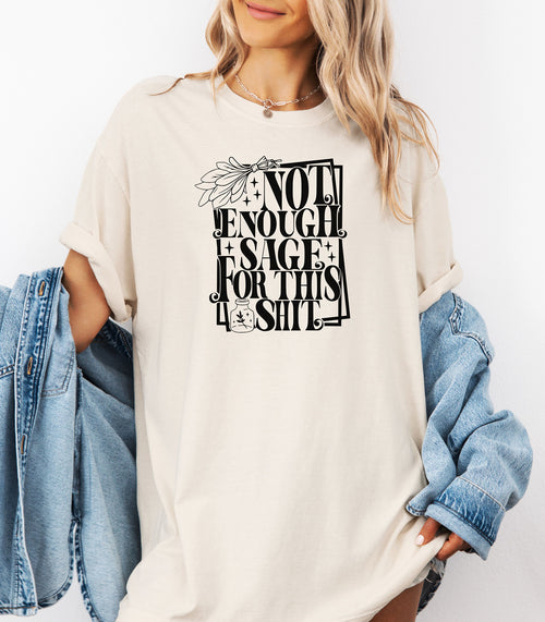 Ivory T-shirt with bold black typography reading “Not Enough Sage For This Shit,” accented with illustrated sage leaves, sparkles, and a small potion jar with a leafy design. Playful and cheeky statement shirt for spiritual, witchy, or humor-loving personalities.