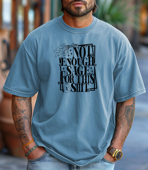 Washed Denim T-shirt with bold black typography reading “Not Enough Sage For This Shit,” accented with illustrated sage leaves, sparkles, and a small potion jar with a leafy design. Playful and cheeky statement shirt for spiritual, witchy, or humor-loving personalities.