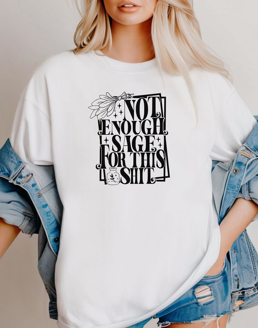 Classic white T-shirt with bold black typography reading “Not Enough Sage For This Shit,” accented with illustrated sage leaves, sparkles, and a small potion jar with a leafy design. Playful and cheeky statement shirt for spiritual, witchy, or humor-loving personalities.
