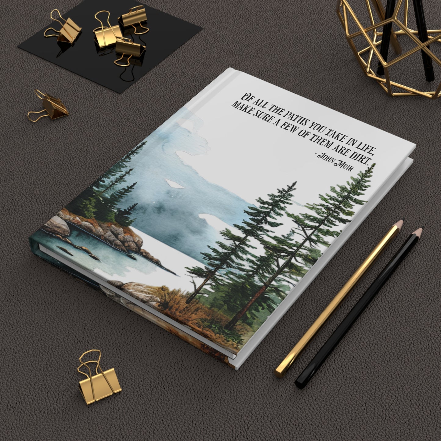 Hardcover journal with nature-themed cover and John Muir quote on a desk with office supplies