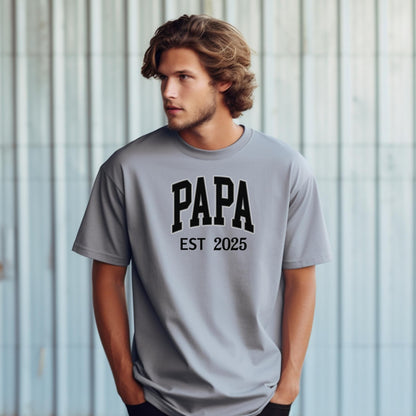 PAPA Est [Year] T-shirt featuring bold collegiate-style lettering with a customizable establishment year. Printed on a soft, relaxed-fit unisex tee in a granite color, this design makes a perfect gift for new grandfathers, Father’s Day, or family celebrations. Ideal for proudly announcing the year someone became 'Papa' while offering comfort and casual style.