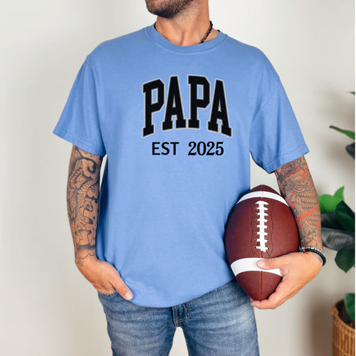 PAPA Est [Year] T-shirt featuring bold collegiate-style lettering with a customizable establishment year. Printed on a soft, relaxed-fit unisex tee in a mystic blue color, this design makes a perfect gift for new grandfathers, Father’s Day, or family celebrations. Ideal for proudly announcing the year someone became 'Papa' while offering comfort and casual style.
