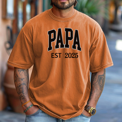 PAPA Est [Year] T-shirt featuring bold collegiate-style lettering with a customizable establishment year. Printed on a soft, relaxed-fit unisex tee in a Yam color, this design makes a perfect gift for new grandfathers, Father’s Day, or family celebrations. Ideal for proudly announcing the year someone became 'Papa' while offering comfort and casual style.