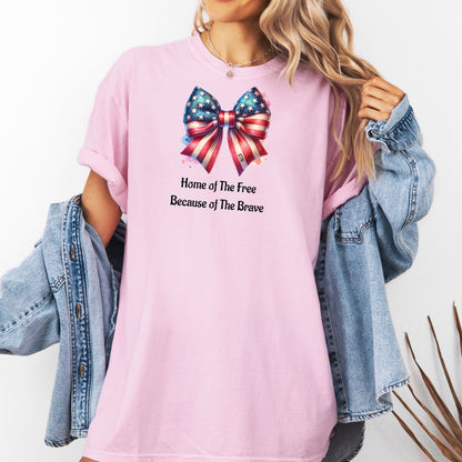 Blossom pink t-shirt featuring a patriotic coquette bow design with stars and stripes in red, white, and blue. Below the bow, the text reads 'Home of The Free Because of The Brave.' A stylish and feminine Holiday shirt, perfect for celebrating Independence Day, parades, and summer festivities.