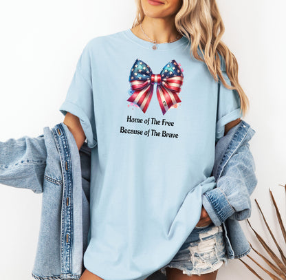 Chambray light blue t-shirt featuring a patriotic coquette bow design with stars and stripes in red, white, and blue. Below the bow, the text reads 'Home of The Free Because of The Brave.' A stylish and feminine Holiday shirt, perfect for celebrating Independence Day, parades, and summer festivities.
