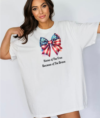White t-shirt featuring a patriotic coquette bow design with stars and stripes in red, white, and blue. Below the bow, the text reads 'Home of The Free Because of The Brave.' A stylish and feminine Holiday shirt, perfect for celebrating Independence Day, parades, and summer festivities.