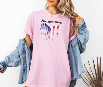 Person wearing a blossom pink T-shirt featuring a heart-shaped design made of dripping red, white, and blue paw prints with star accents. Above the heart, the text reads “Paws & Stripes Furever,” blending patriotic pride with a love for pets, making it a perfect shirt for animal lovers and USA enthusiasts.
