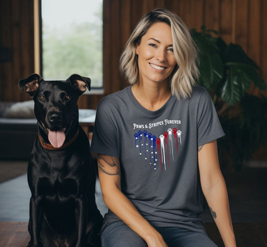 A person wearing a pepper T-shirt featuring a heart-shaped design made of dripping red, white, and blue paw prints with star accents. Above the heart, the text reads “Paws & Stripes Furever,” blending patriotic pride with a love for pets, making it a perfect shirt for animal lovers and USA enthusiasts.