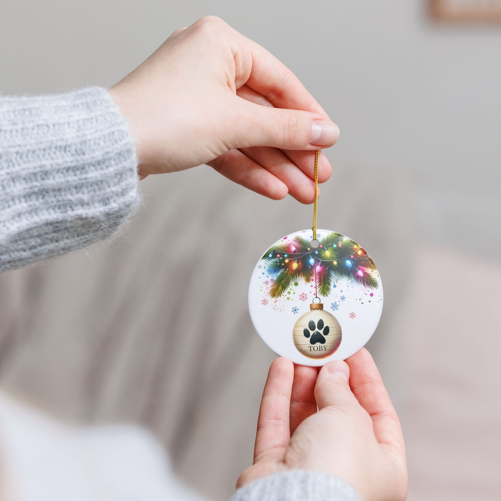 Person holding a Christmas ornament with a paw print design and pet's name.