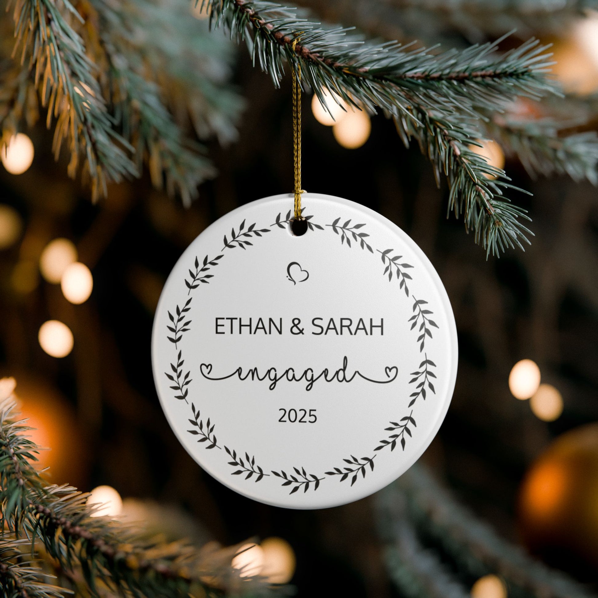 Round ornament with 'Ethan & Sarah engaged 2025' text hanging on a Christmas tree.