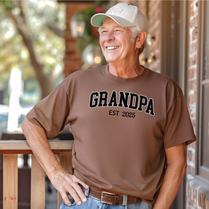 Espresso t-shirt featuring a bold collegiate-style 'GRANDPA EST [Year]' design in black and white lettering. Perfect gift for new grandfathers to celebrate the year they became a grandpa. A thoughtful, casual, and comfortable shirt ideal for Father's Day, family gatherings, or everyday wear.