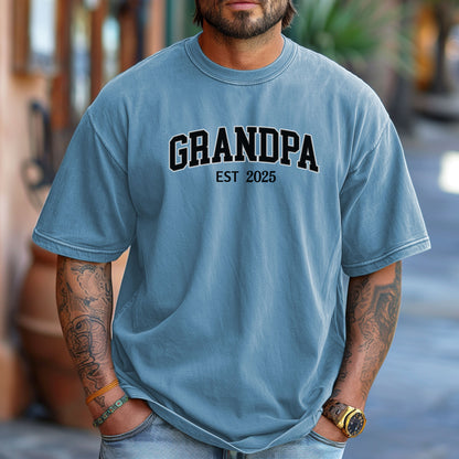 Washed Denim t-shirt featuring a bold collegiate-style 'GRANDPA EST [YEAR]' design in black and white lettering. Perfect gift for new grandfathers to celebrate the year they became a grandpa. A thoughtful, casual, and comfortable shirt ideal for Father's Day, family gatherings, or everyday wear.