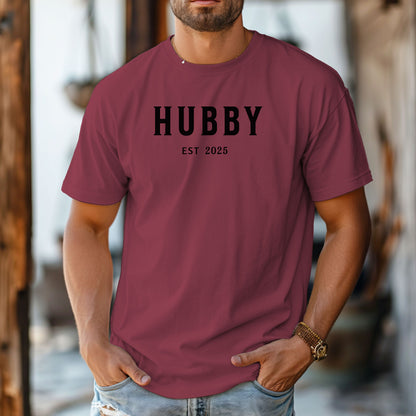Hubby Est [Year] design printed on a Chili unisex t-shirt. The shirt features bold black capital letters spelling 'HUBBY' with 'EST [Year]' in smaller text below. Perfect for newlyweds, anniversaries, or wedding gifts, this casual and modern design celebrates marriage in a simple, stylish way. 