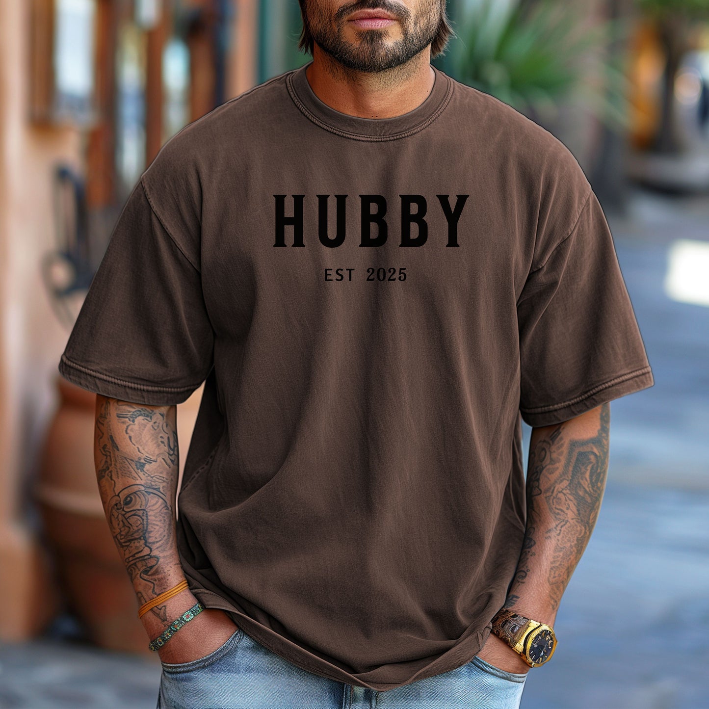 Hubby Est [Year] design printed on a Espresso unisex t-shirt. The shirt features bold black capital letters spelling 'HUBBY' with 'EST [Year]' in smaller text below. Perfect for newlyweds, anniversaries, or wedding gifts, this casual and modern design celebrates marriage in a simple, stylish way. 