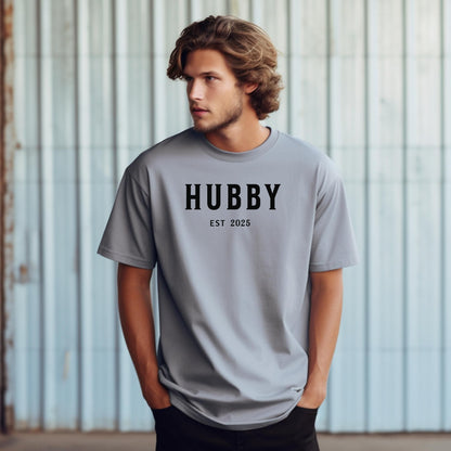 Hubby Est [Year] design printed on a Granite unisex t-shirt. The shirt features bold black capital letters spelling 'HUBBY' with 'EST [Year]' in smaller text below. Perfect for newlyweds, anniversaries, or wedding gifts, this casual and modern design celebrates marriage in a simple, stylish way. 