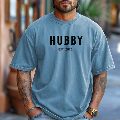 Hubby Est [Year] design printed on a Washed Denim unisex t-shirt. The shirt features bold black capital letters spelling 'HUBBY' with 'EST [Year]' in smaller text below. Perfect for newlyweds, anniversaries, or wedding gifts, this casual and modern design celebrates marriage in a simple, stylish way. 