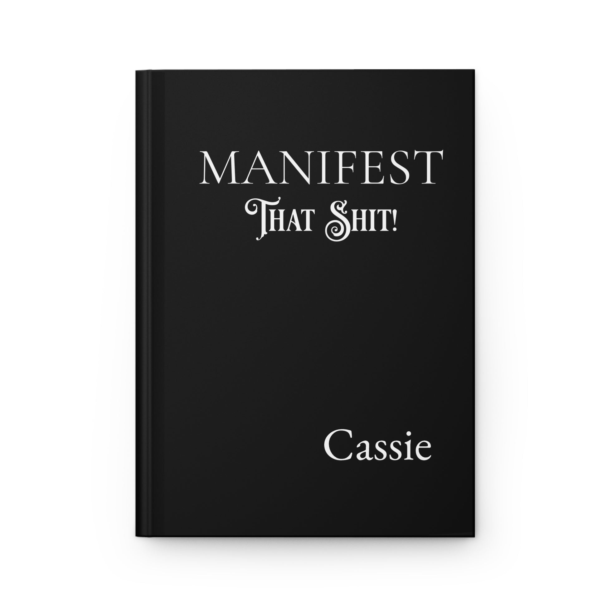 Black hardcover journal with 'MANIFEST THAT SHIT!' and name on a white background