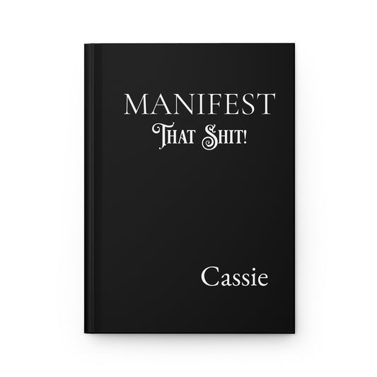 Black hardcover journal with 'MANIFEST THAT SHIT!' and name on a white background