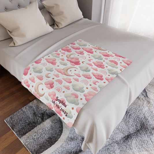 Personalized baby blanket with clouds, stars, and pink rainbow pattern on a bed.