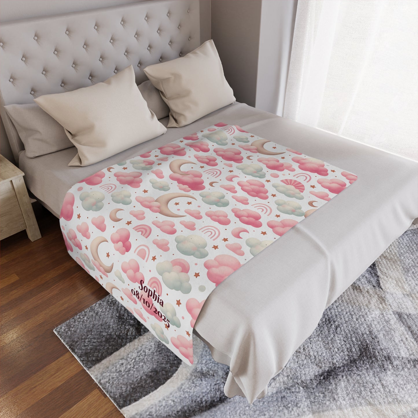 Personalized baby blanket with clouds, stars, and pink rainbow pattern on a bed.