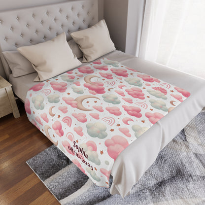 Personalized baby blanket with clouds, stars, and pink rainbow pattern on a bed.