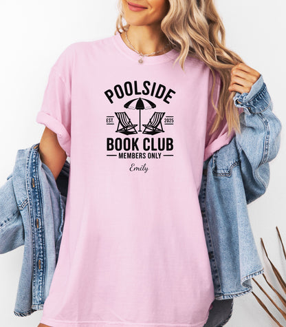 Person wearing a Blossom pink T-shirt featuring a "Poolside Book Club Members Only" design with two lounge chairs and an umbrella graphic, personalized with the name you choose.