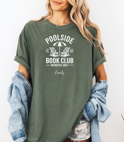 Person wearing a Hemp color T-shirt featuring a "Poolside Book Club Members Only" design with two lounge chairs and an umbrella graphic, personalized with the name you choose.