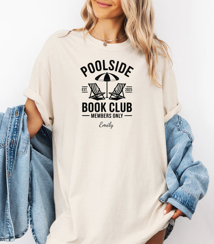 Person wearing an Ivory T-shirt featuring a "Poolside Book Club Members Only" design with two lounge chairs and an umbrella graphic, personalized with the name you choose.