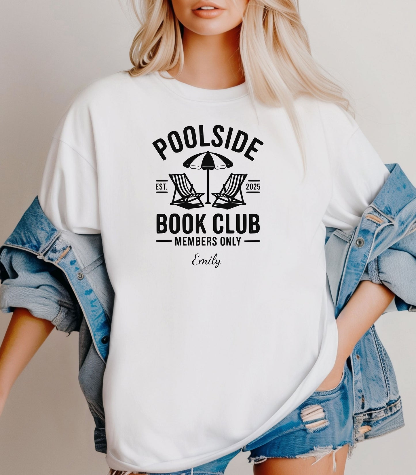 Person wearing a White T-shirt featuring a "Poolside Book Club Members Only" design with two lounge chairs and an umbrella graphic, personalized with the name you choose.