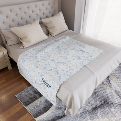 Personalized Rocking Horse Minky blanket with blue chinoiserie patterns and 'Oliver' text on a bed in a bedroom.