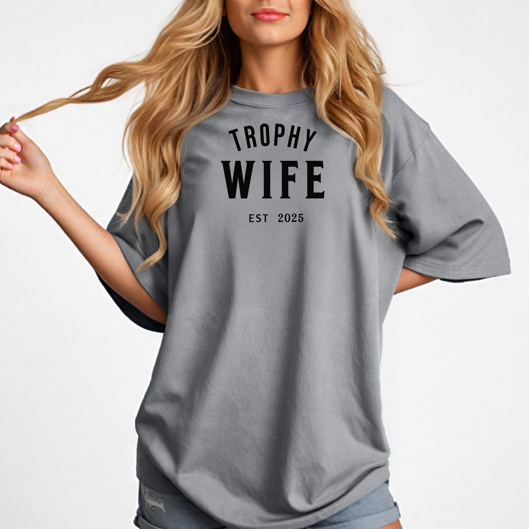 "Trophy Wife Est [Year] design on a granite unisex t-shirt. The shirt features bold black lettering with 'TROPHY WIFE' in large uppercase letters and 'EST [Year]' below in smaller text. A fun and stylish design perfect for newlyweds, anniversaries, or bridal gifts, celebrating marriage with a confident modern look. Modeled in a casual, relaxed fit style."