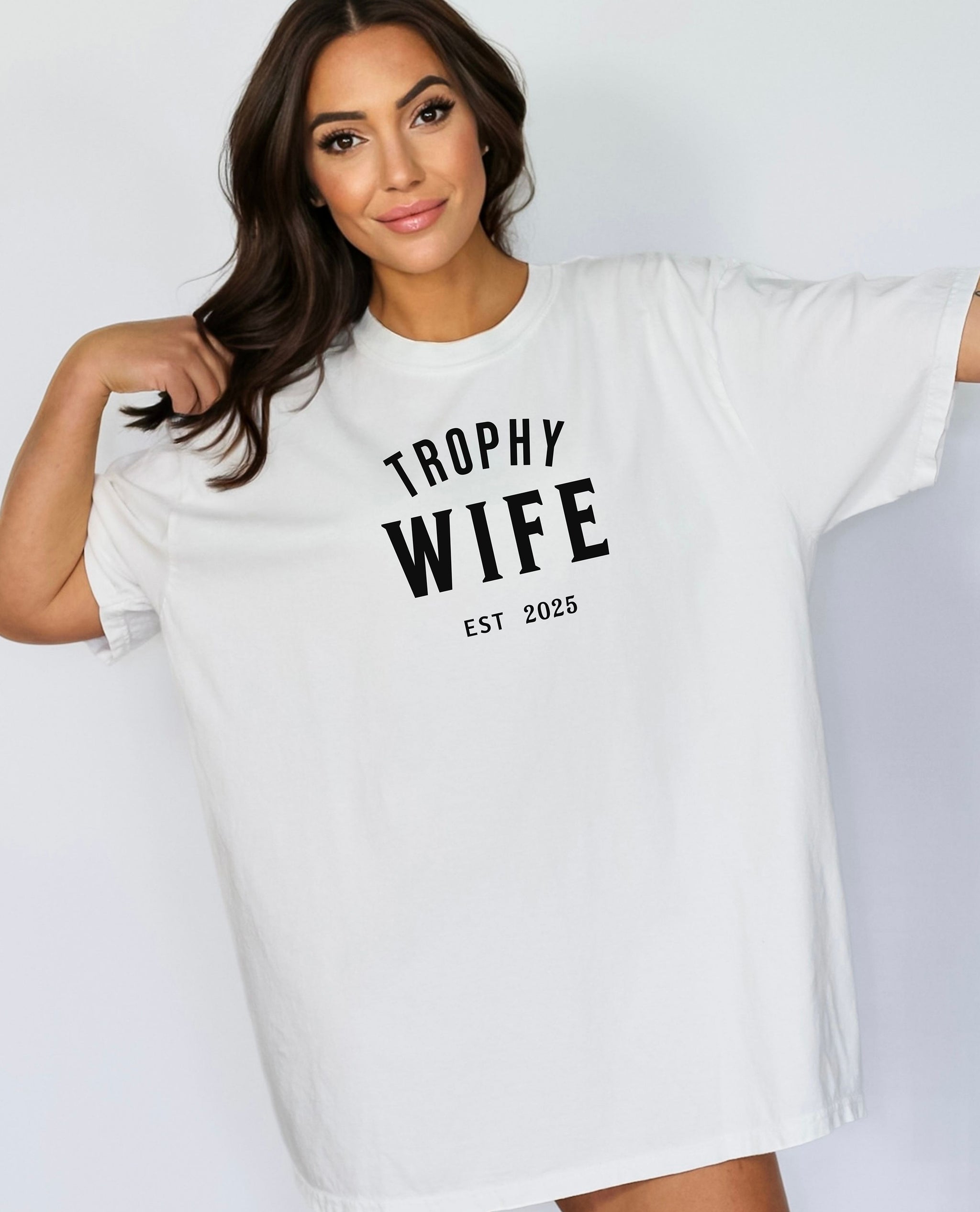 "Trophy Wife Est [Year] design on a white unisex t-shirt. The shirt features bold black lettering with 'TROPHY WIFE' in large uppercase letters and 'EST [Year]' below in smaller text. A fun and stylish design perfect for newlyweds, anniversaries, or bridal gifts, celebrating marriage with a confident modern look. Modeled in a casual, relaxed fit style."