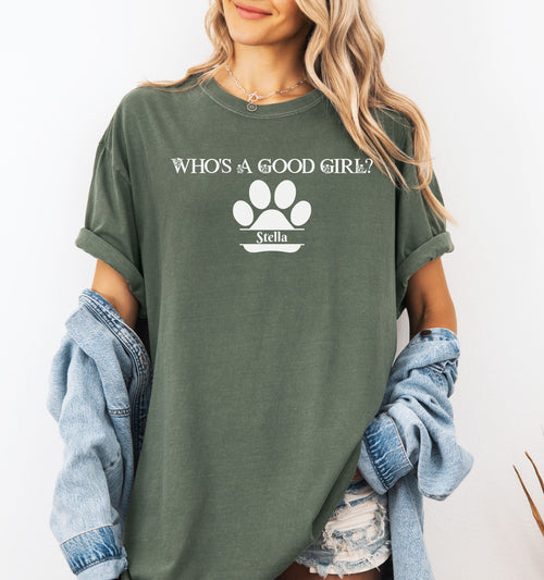 Woman wearing a Hemp color t-shirt that reads “Who’s a Good Girl?” above a white paw print graphic with the name “Stella”. The shirt is a playful and heartwarming tribute to a beloved pet—perfect for dog Moms and puppy lovers.
