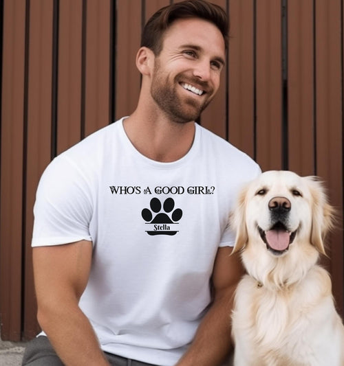 Man wearing an White t-shirt that reads “Who’s a Good Girl?” above a black paw print graphic with the name “Stella”.  Sitting with a golden retriever, the shirt is a playful and heartwarming tribute to a beloved pet—perfect for dog Dads and puppy lovers.