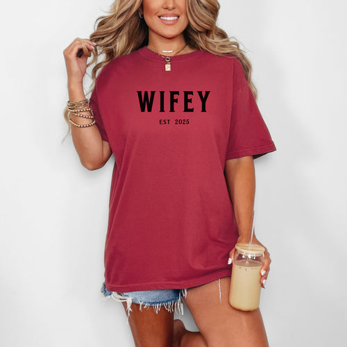 Chili T-shirt with the text "WIFEY EST 2025" in bold black lettering, celebrating a newlywed or engaged status. The modern minimalist design makes it perfect for brides, honeymoon outfits, or casual newlywed style.  Ideal for wedding gifts, bridal showers, or anniversary celebrations.