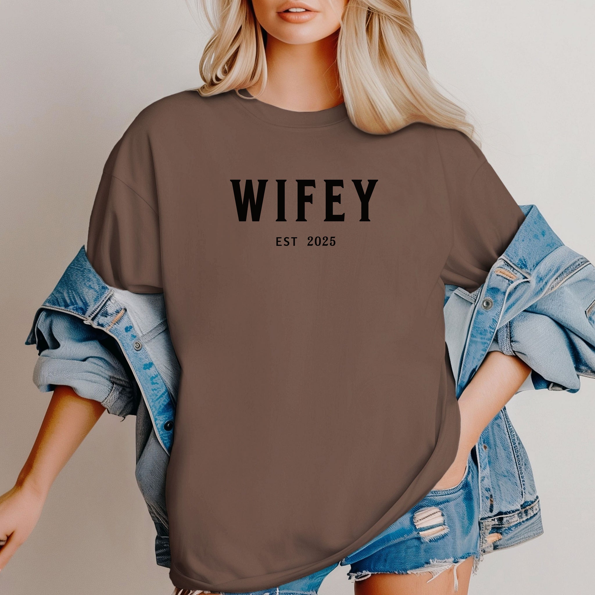 Espresso T-shirt with the text "WIFEY EST 2025" in bold black lettering, celebrating a newlywed or engaged status. The modern minimalist design makes it perfect for brides, honeymoon outfits, or casual newlywed style.  Ideal for wedding gifts, bridal showers, or anniversary celebrations.
